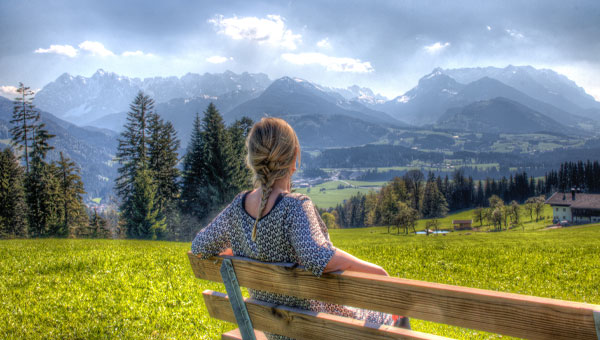 Frau auf einer Bank mit Sicht auf die Alpen