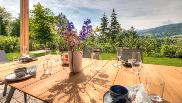 Tisch auf der Terrasse/ im garten mit Aussicht auf die Alpen und Büsche welche den Garten einrahmen